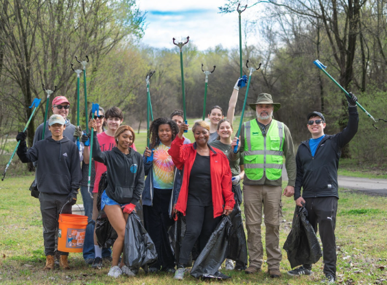 A group of diverse volunteers with Volunteer Odyssey holding trash pickers and bags proudly posing after a community cleanup event in a park.